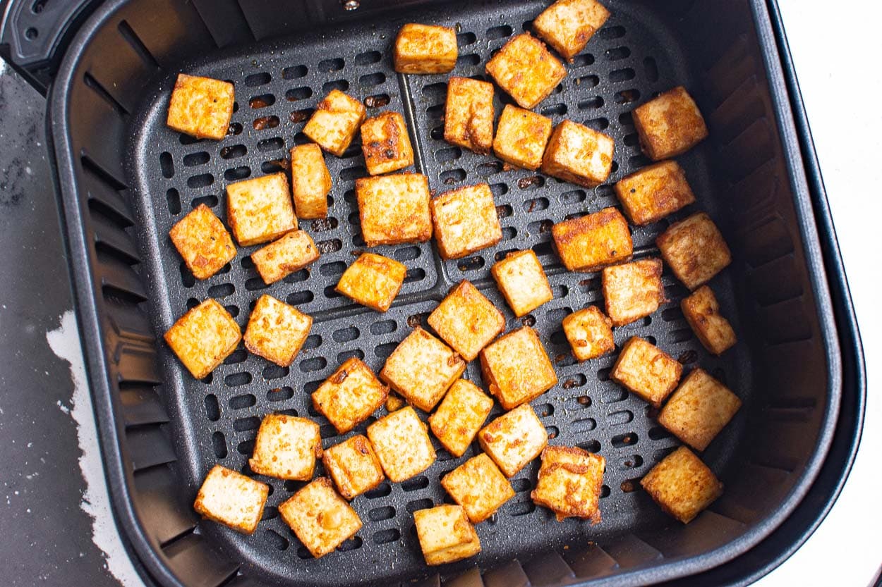 Cooked tofu cubes in air fryer basket.