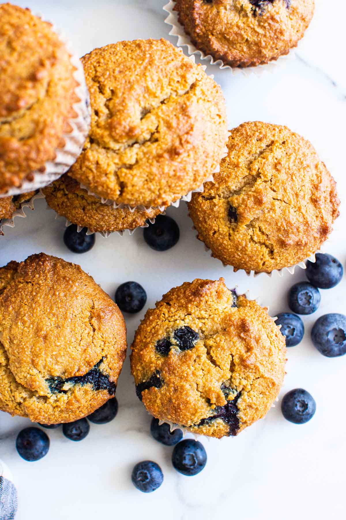 Healthy almond flour blueberry muffins on a counter, some stacked, with fresh blueberries.