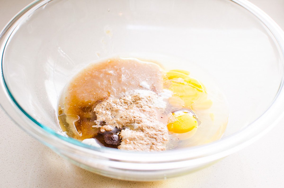 A mixing bowl with eggs, applesauce, maple syrup, oil, extract, baking powder, soda, cinnamon and salt.