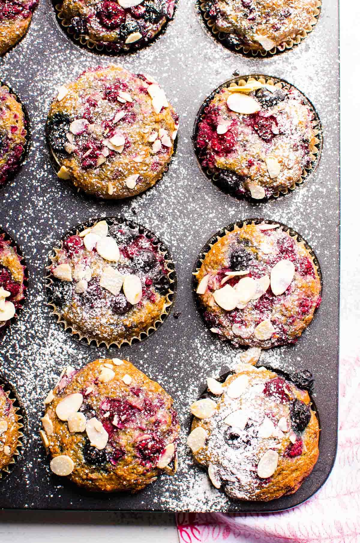 Almond berry muffins in a muffin tin sprinkled with sliced almonds and sugar.