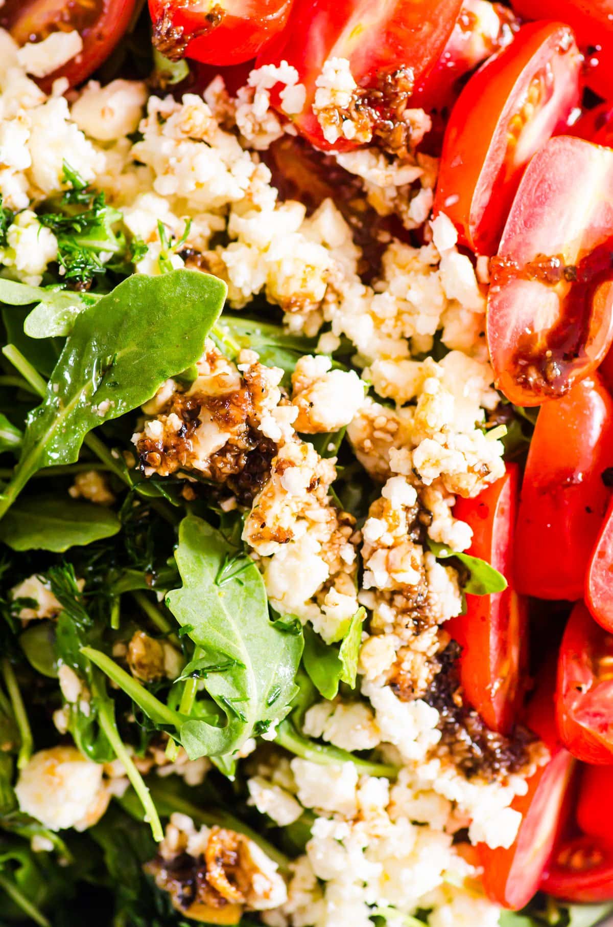 Close up of arugula feta salad with tomatoes and balsamic vinaigrette drizzled on top.