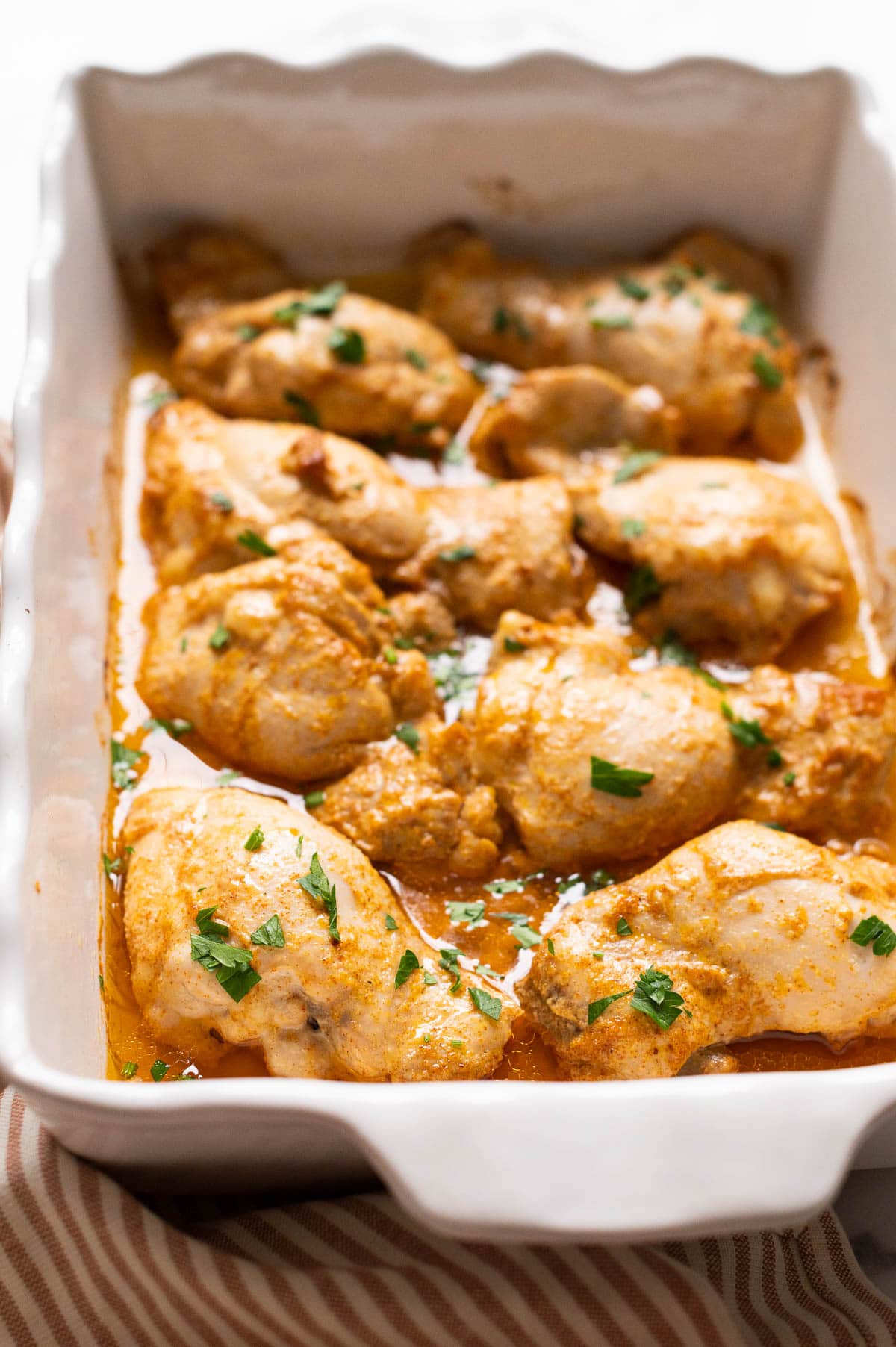 Side view of baked skinless chicken thighs with cooking juices in a baking dish.