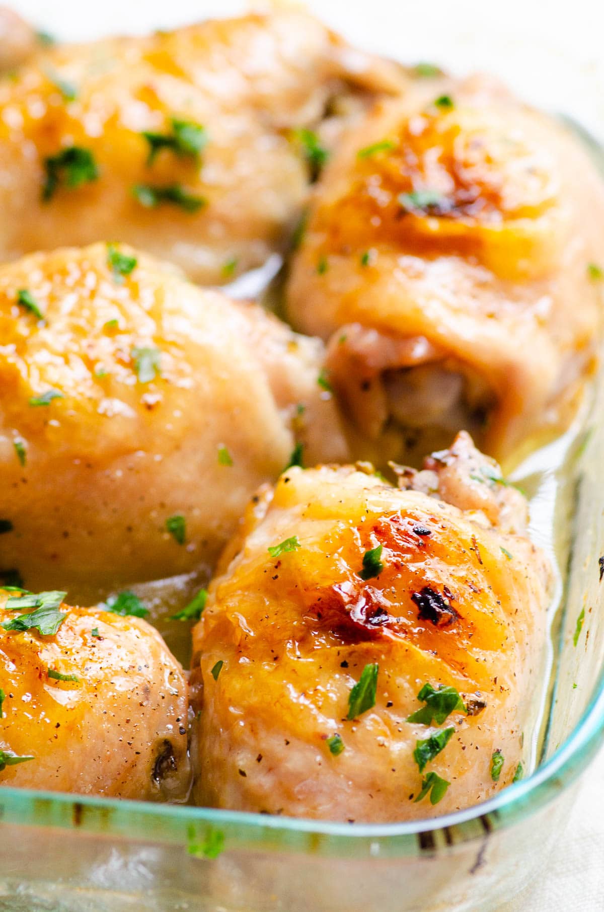 Close up side view of baked chicken thighs in a glass baking dish.