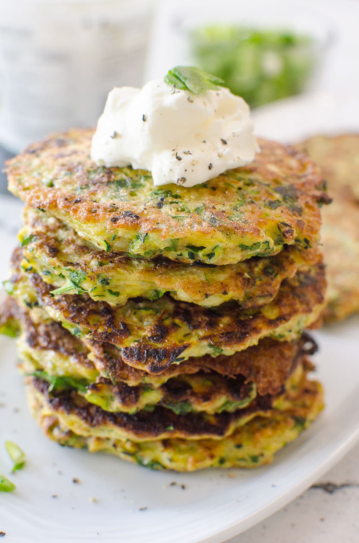 A stack of baked zucchini fritters with a dollop of sour cream on top.