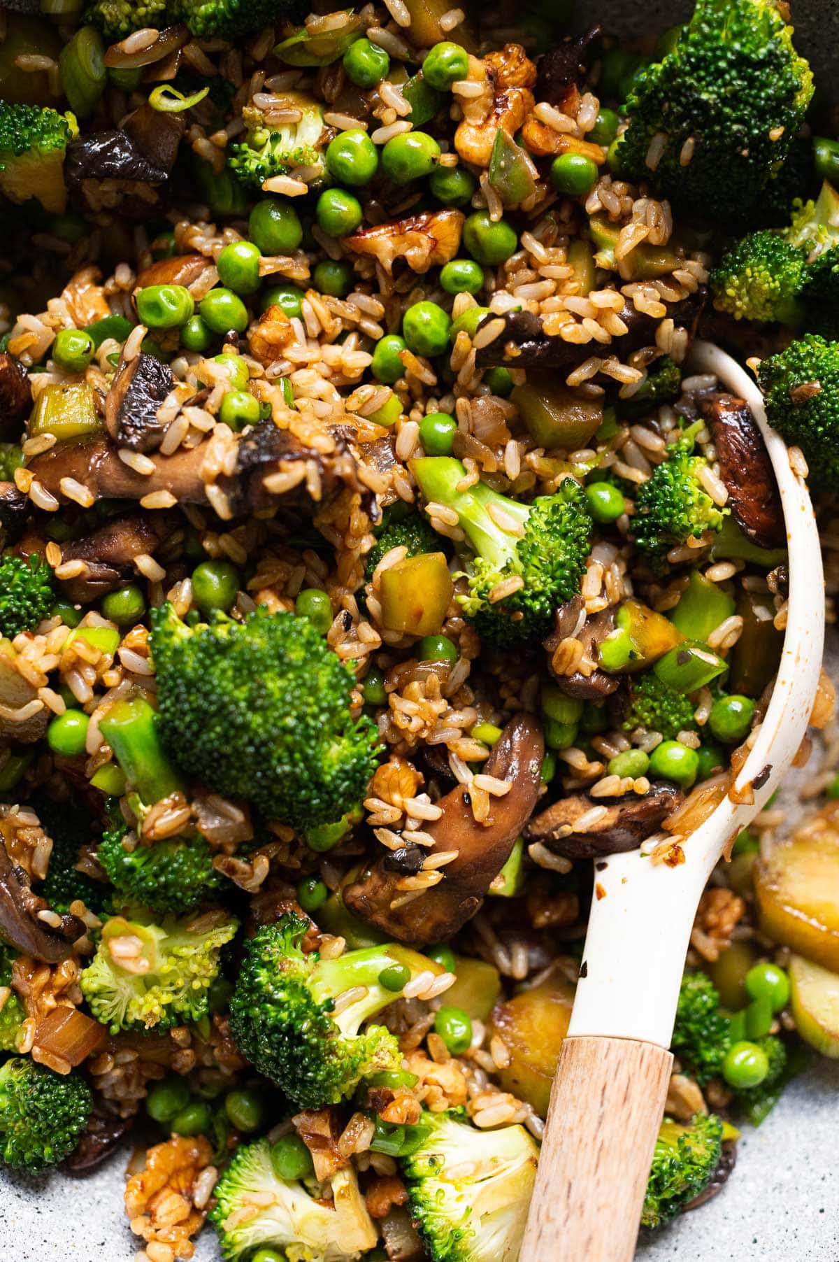 Close up of broccoli and mushroom stir fry recipe with peas, green onions and brown rice.