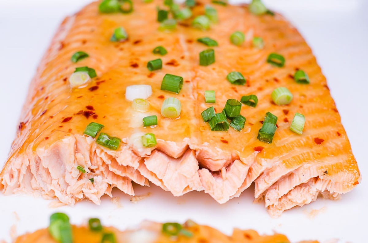 A piece of salmon coated in Thai sweet chili sauce and garnished with green onion showing texture inside.