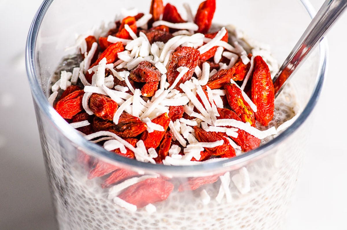 Chia pudding in a glass with coconut flakes, goji berries and spoon.