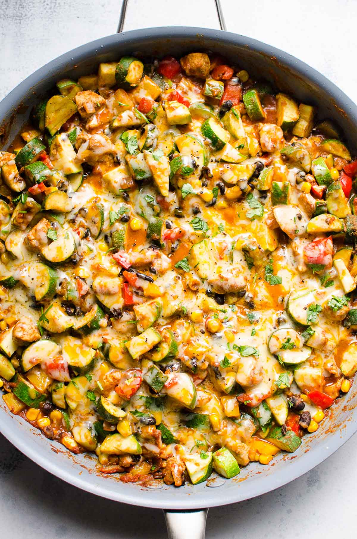 Tex Mex chicken and zucchini recipe with melted cheese and cilantro in blue skillet.
