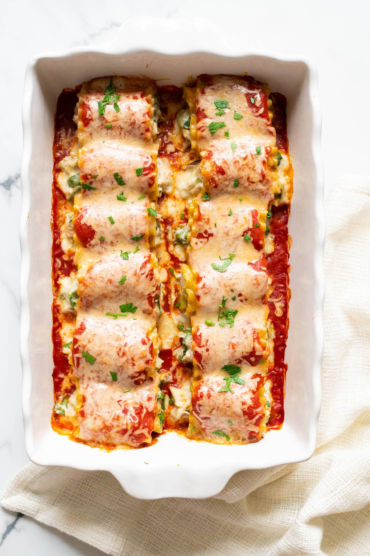 Twelve chicken lasagna roll-ups garnish with parsley in a baking dish.