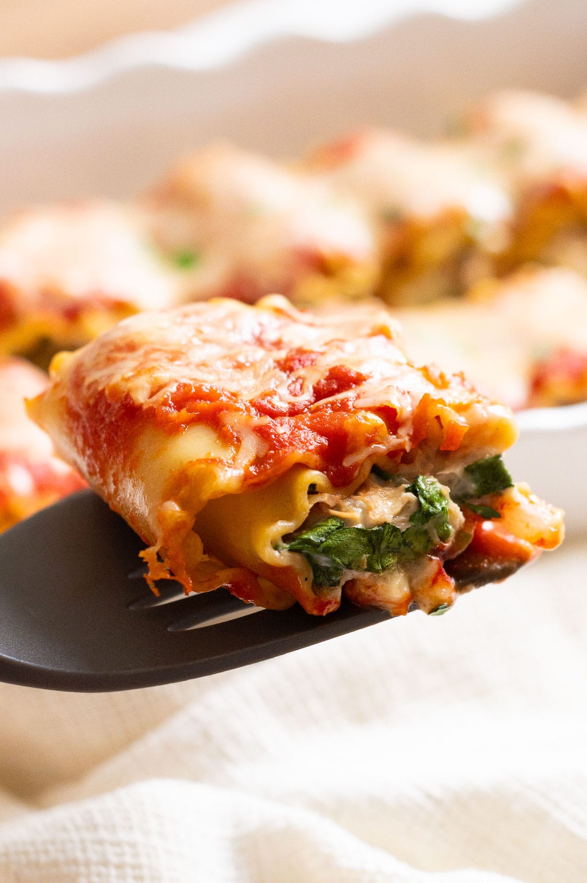 Chicken lasagna roll with artichokes and spinach on a spatula.