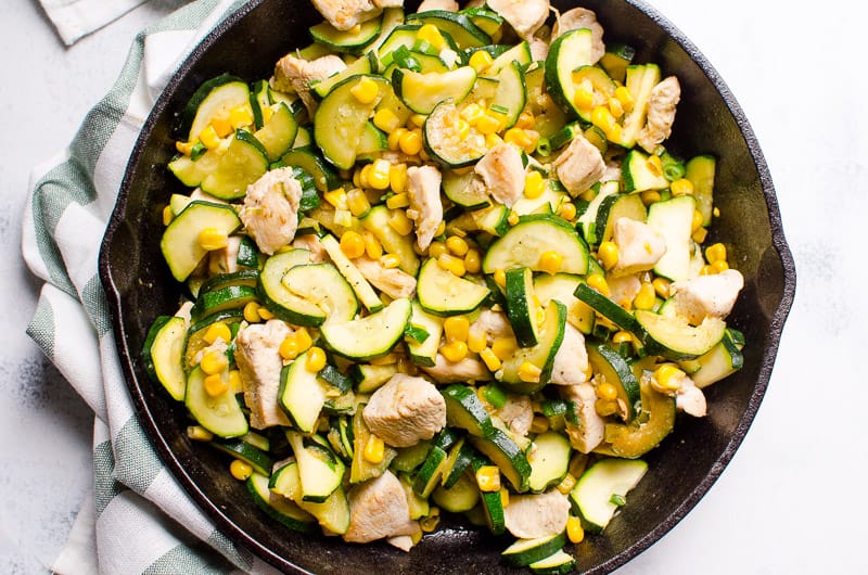 Chicken with zucchini, corn and garlic in a cast iron skillet. Linen towel near it.