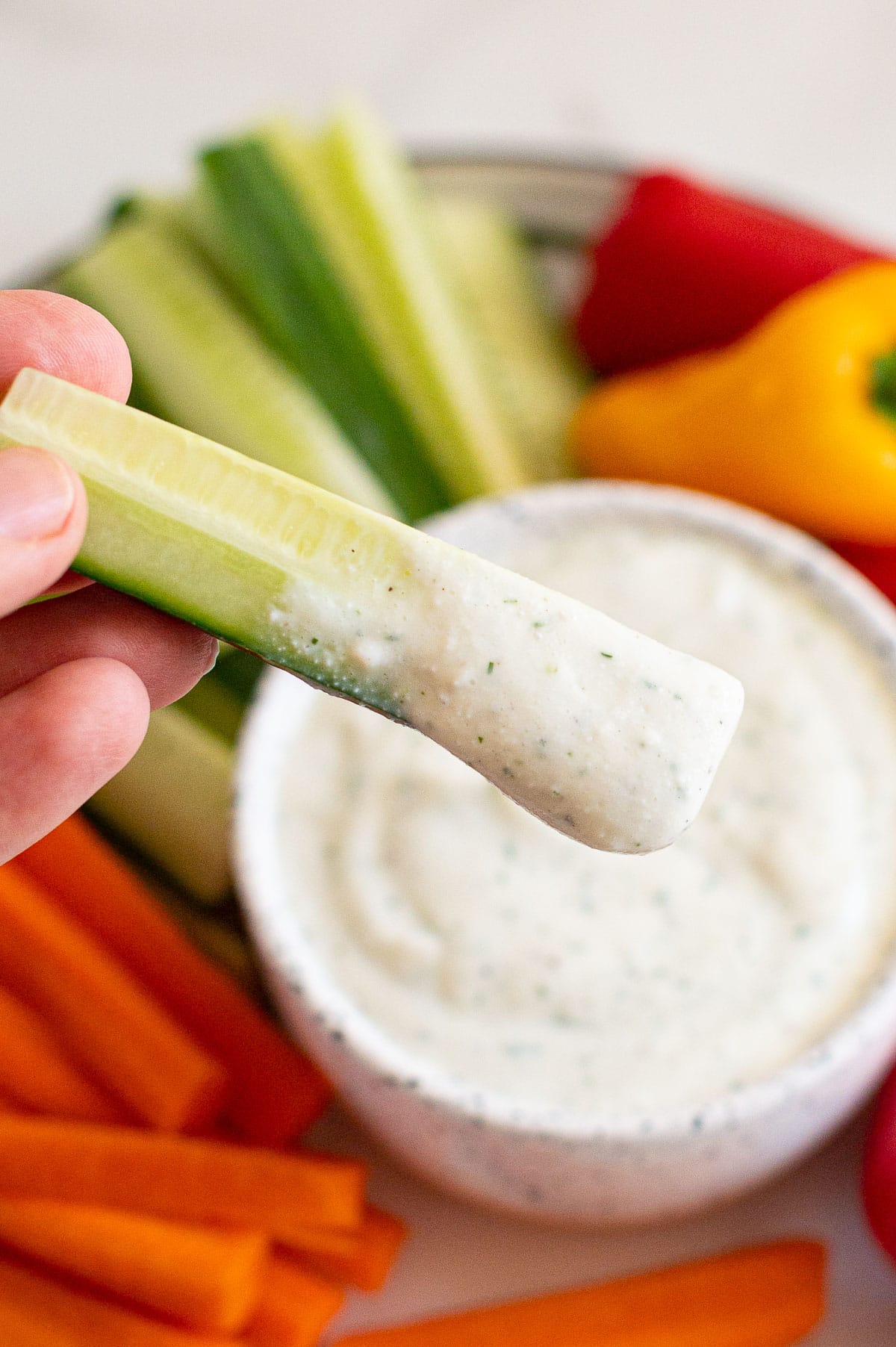 Person holding cucumber stick dipped into ranch dip.