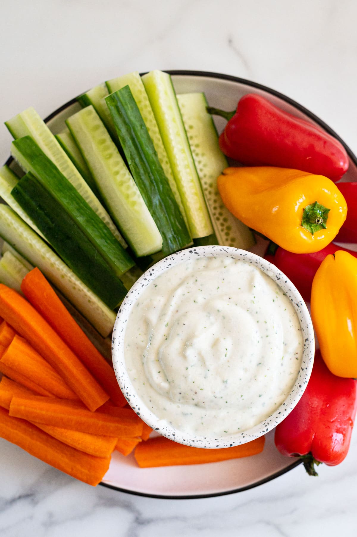 Cottage cheese ranch dip in a bowl served with cucumbers, carrots and bell peppers on a plate.