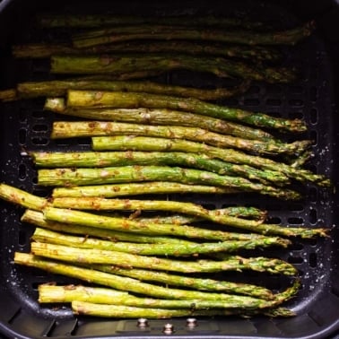 Cooked air fryer asparagus in the basket of air fryer.