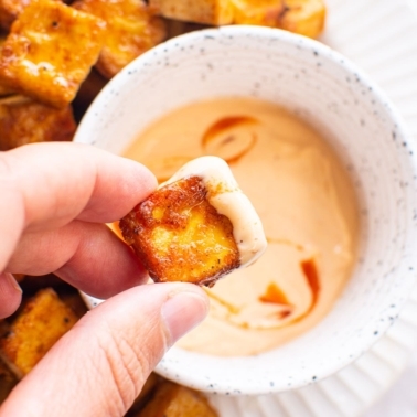 Hand holding air fryer tofu dipped in spicy mayo.
