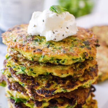 Baked zucchini fritters stacked with dollop of sour cream on top on a plate.