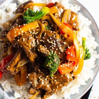 Beef stir fry recipe served over white rice and garnish with sesame seeds.