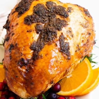 Bone in turkey breast roast with orange slices and fresh cranberries on a platter.