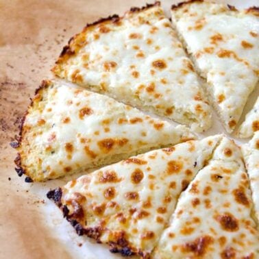 Cauliflower pizza crust with cheese sliced on parchment paper.