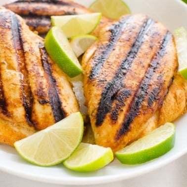 Chili lime chicken breasts served with lime slices on a plate.