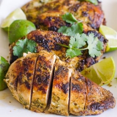 Sliced cilantro lime chicken breasts garnished with cilantro and limes.
