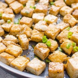 Fried tofu cubes garnished with sesame seeds and green onion in a skillet.