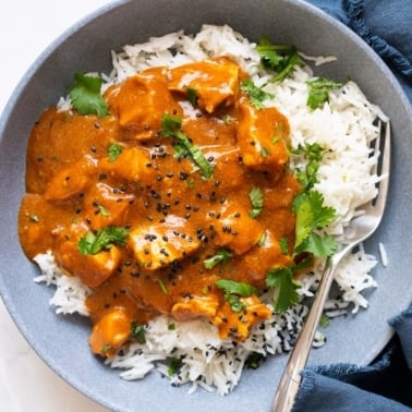 Crock pot butter chicken served over rice and garnished with cilantro and sesame seeds.
