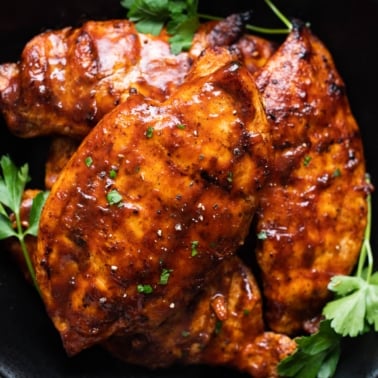 Grilled BBQ chicken breasts garnished with parsley served on black plate.