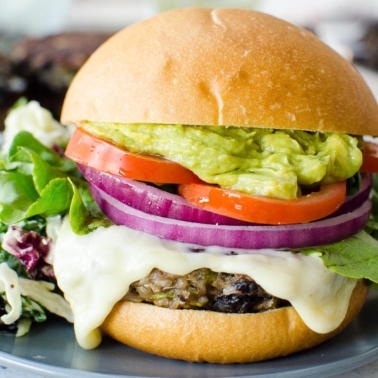 Healthy black bean burgers on bun with cheese, onion, tomato and guacamole.