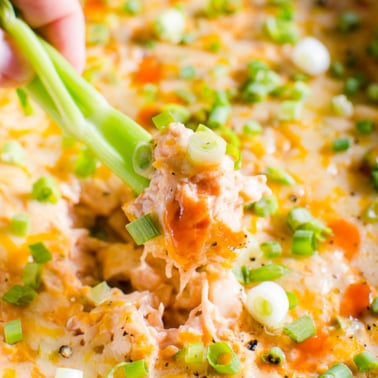 Healthy buffalo chicken dip in a dish with celery stick being dipped into it.