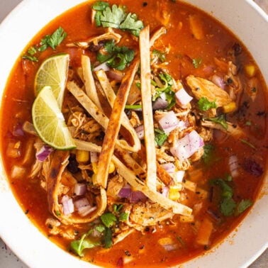 Healthy chicken tortilla soup served with tortilla strips, cilantro and red onion in a bowl with a spoon.