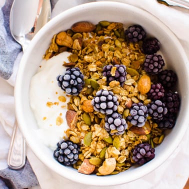 Healthy granola in a bowl with yogurt and frozen blackberries.