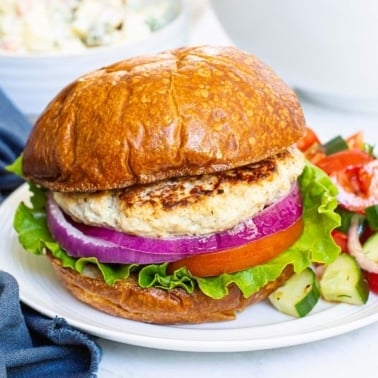 Healthy ground chicken burger with lettuce, tomato and red onion on white plate.