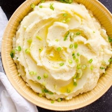 Healthy mashed potatoes with melted butter, pepper and green onion on top.