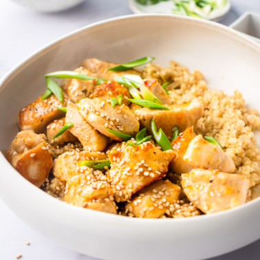 Healthy orange chicken garnished with green onion and served on top of quinoa in a bowl.