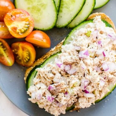 Healthy tuna salad on a toast garnished with red onion on blue plate with tomatoes and cucumbers.