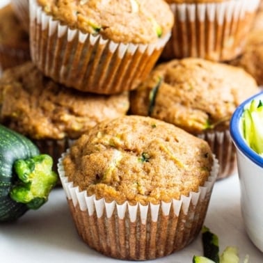 Healthy zucchini muffins some stacked with a fresh zucchini.