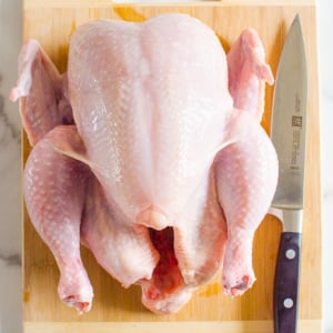 Whole chicken on a cutting board with a knife.