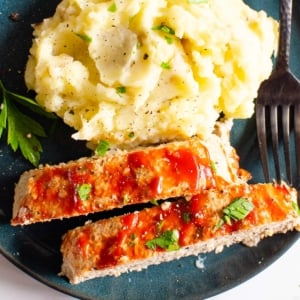 Instant pot meatloaf and mashed potatoes garnished with parsley and served on a plate with a fork.