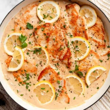 Lemon garlic chicken in creamy sauce with slices of lemon and parsley in a skillet.