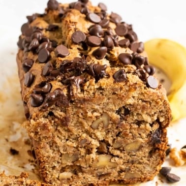 Sliced oat flour banana bread with walnuts and chocolate chips on parchment paper.