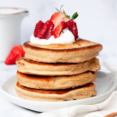 A stack of oat flour pancakes topped with sour cream and strawberries on a plate.