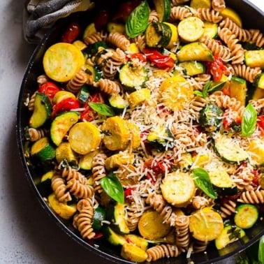 Pasta with zucchini, tomatoes, parmesan cheese and fresh basil in a skillet.