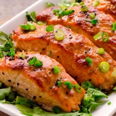 Peanut butter salmon served on a bed of greens and garnished with black sesame seeds and green onions.