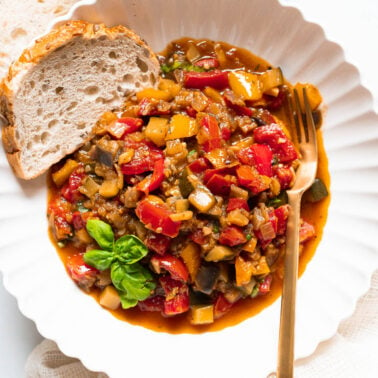Ratatouille served in a bowl with slice of bread and garnished with basil. Fork on the side.