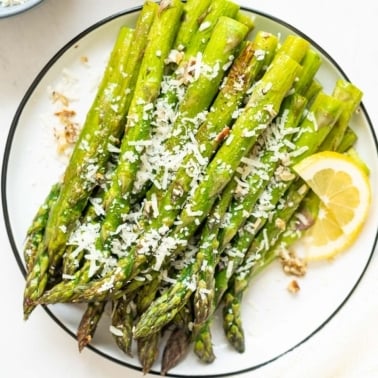 Roasted asparagus garnished with Parmesan cheese and lemon on a plate.