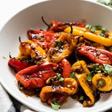 A bowl with roasted mini bell peppers garnished with garlic and basil.