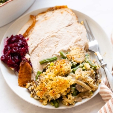 A plate with sliced turkey breast, green bean casserole and cranberry sauce.