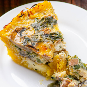 A slice of spaghetti squash quiche with kale and mushrooms with a fork on a plate.