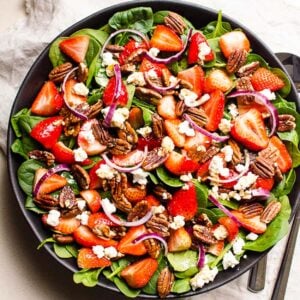 Strawberry spinach salad with feta cheese in a bowl with utensils.